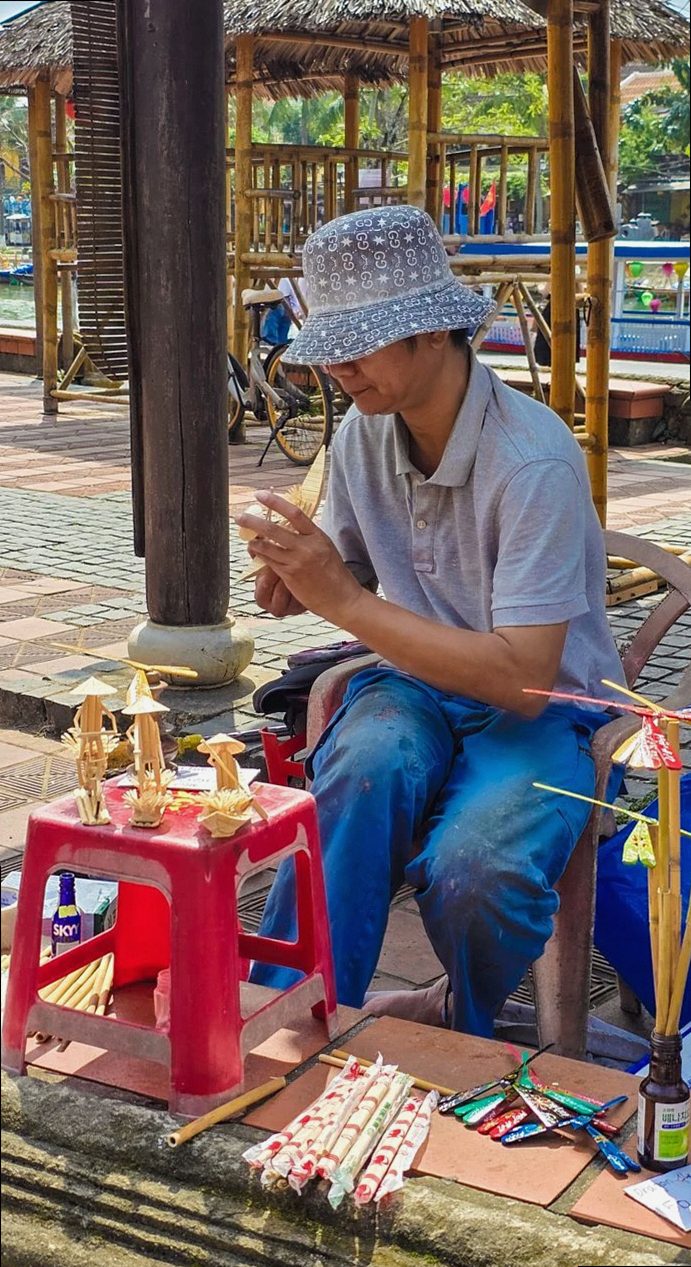 A skilled street artisan creates intricate bamboo toys in a vibrant outdoor market in Vietnam.